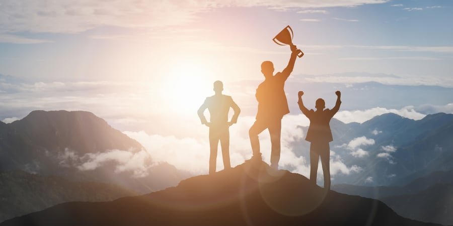 Businessmen-celebrating-with-trophy-on-mountaintop-goal-setting